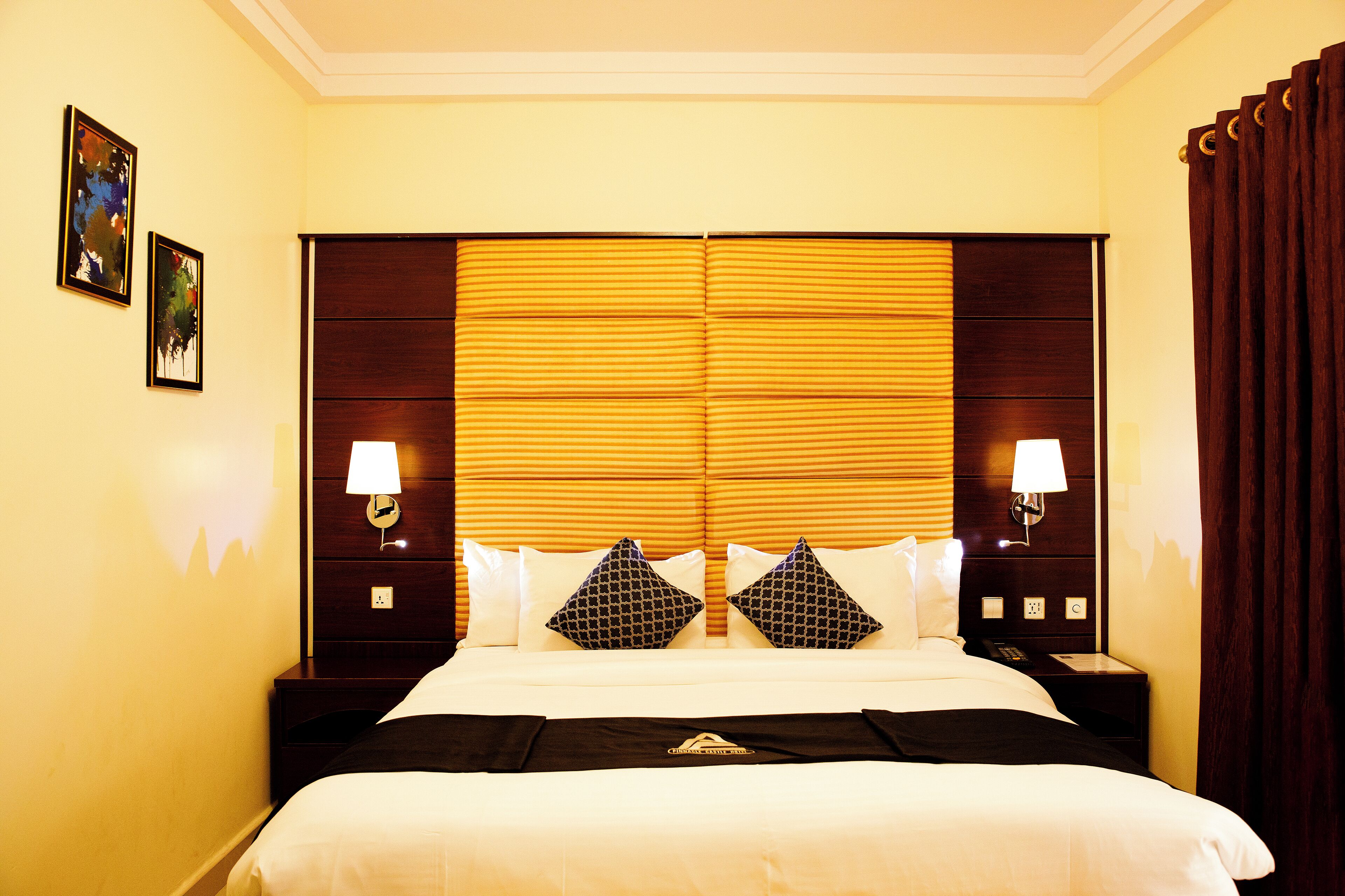 A hotel room with a large bed, two bedside tables with lamps, and a headboard with a striped pattern.
