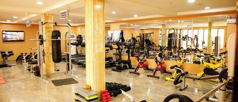 Ett gym med olika typer av träningsredskap, en tv och en träpelare.
