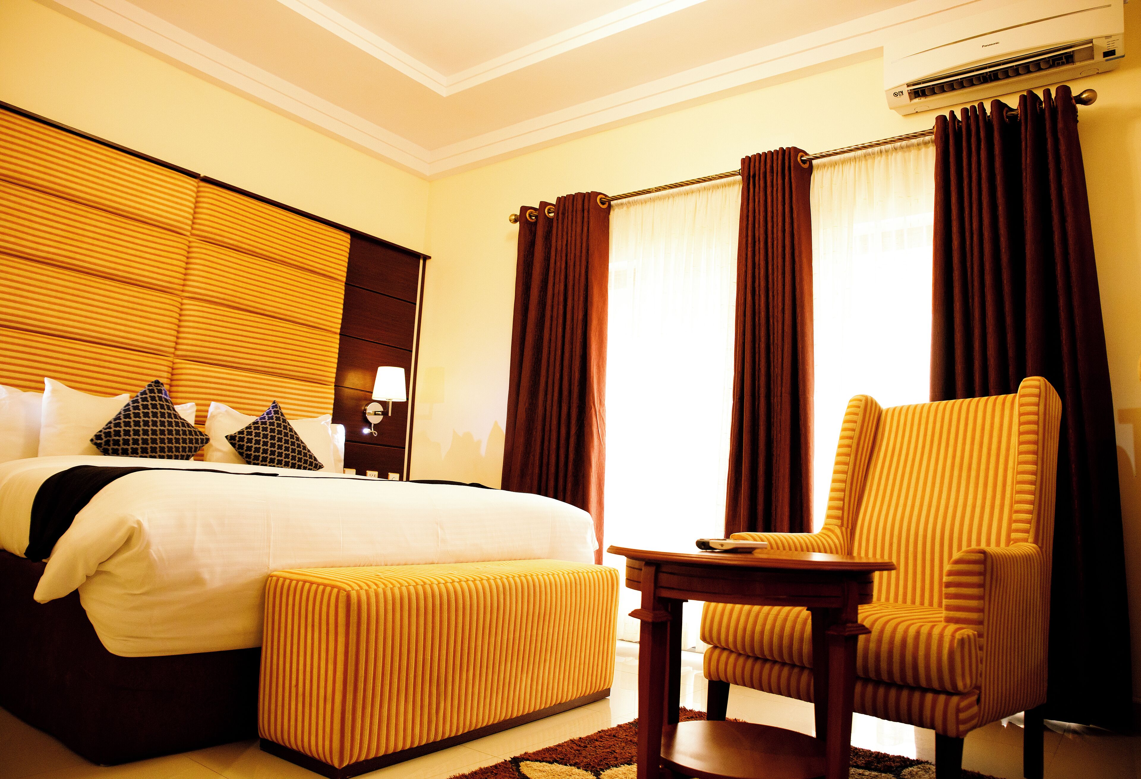 A hotel room with a bed, a chair, a table, and an air conditioning unit.