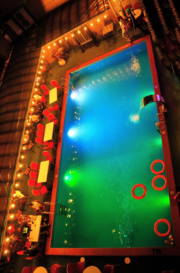 A pool table with a green felt surface, surrounded by red chairs and tables.