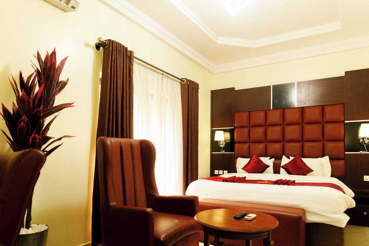 A hotel room with a large bed, a brown leather chair, a small round table, and a potted plant.