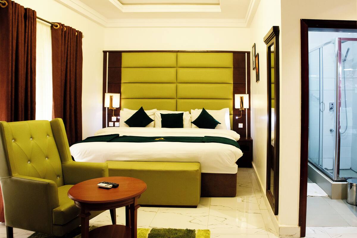 A hotel room with a large bed, a green armchair, a small table, and a view of the outside through a door.