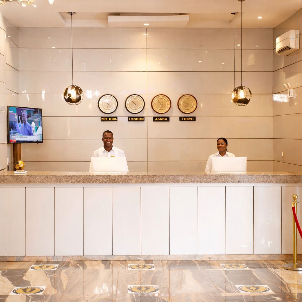 Un mostrador de recepción de hotel con relojes que marcan diferentes husos horarios, una pantalla de televisión y un piso de mármol.