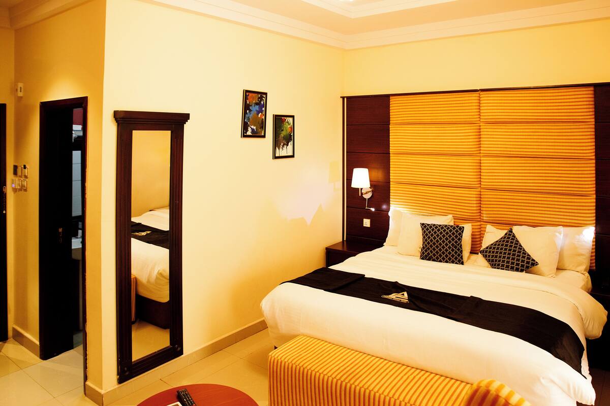A hotel room with a large bed, a bedside table with a lamp, a mirror, and two framed pictures on the wall.