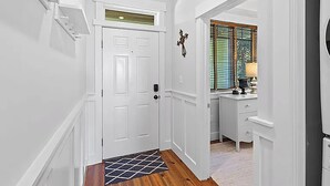 Un couloir avec une porte blanche, un petit tapis et un bureau avec une lampe.