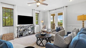 Un salon spacieux doté d’un ventilateur de plafond, d’un téléviseur à écran plat, d’une table à manger et de sièges confortables.