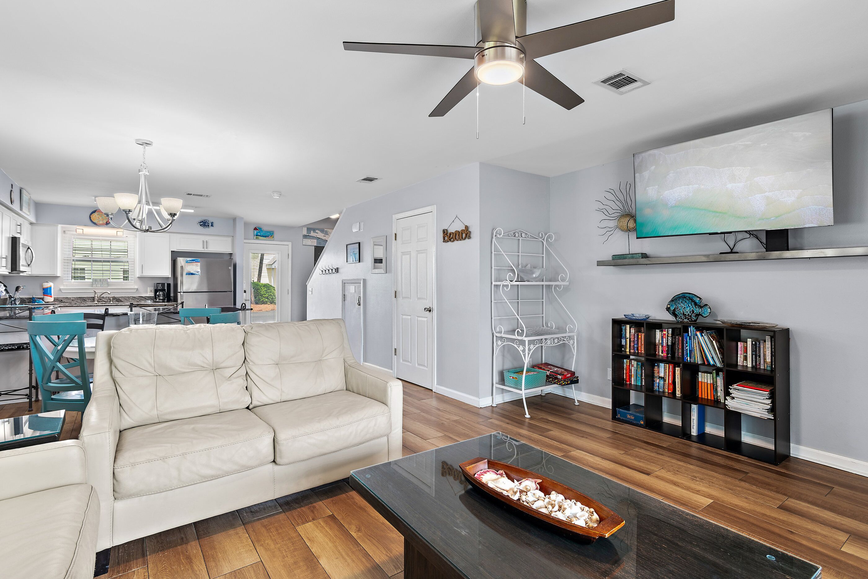 A modern living room with a sofa, coffee table, TV, bookshelf, and a ceiling fan.