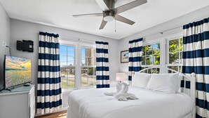 Ein Hotelzimmer mit Bett, Deckenventilator, Fernseher und einem fensterbelaubten Fenster.