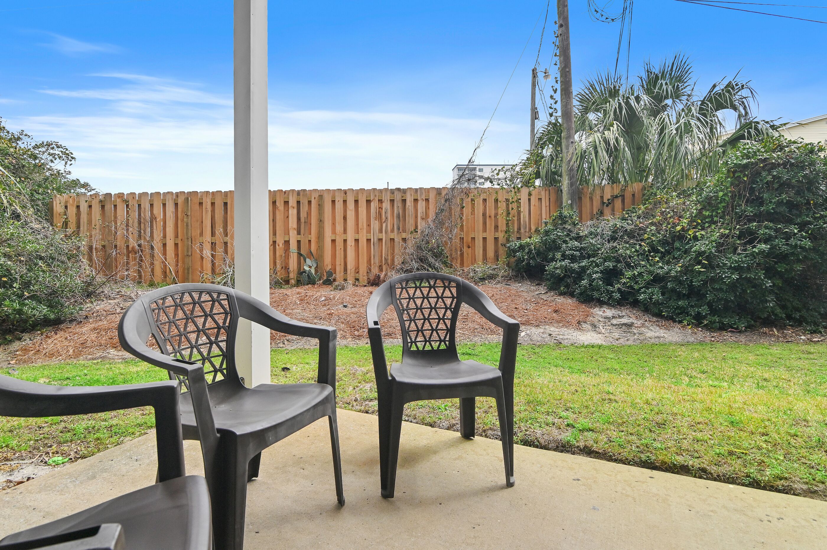 A patio area with two chairs and a concrete floor, surrounded by a wooden fence and greenery.