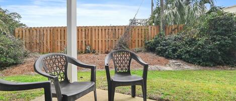 A patio area with two chairs and a concrete floor, surrounded by a wooden fence and greenery.