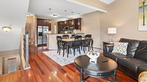 A modern living room with a black leather sofa, a dining area with wooden chairs, and a kitchen in the background. - ☀️100 feet to Beach | Pool | Multiple Balconies and Patio | Beach Pointe 301☀️ (Destin)