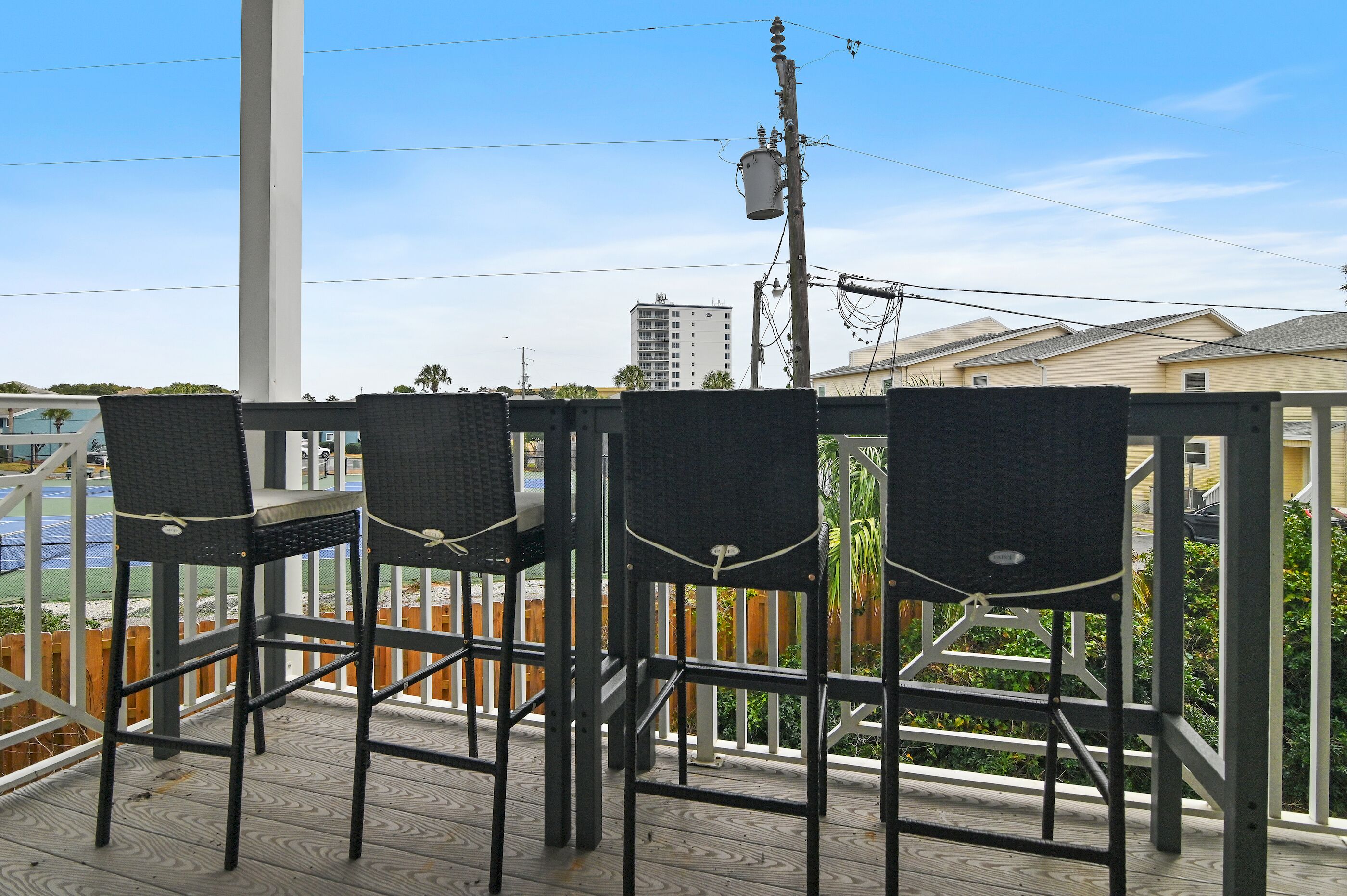 Een balkon met rieten stoelen en een tafel, met uitzicht op een omheind gebied met gebouwen op de achtergrond.
