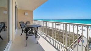 Un balcon avec une table et des chaises, donnant sur une plage et offrant une vue dégagée sur l’océan.