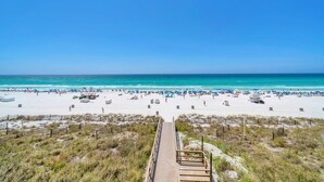 Une plage avec une promenade en bois menant au rivage, une plage de sable et un ciel bleu clair.