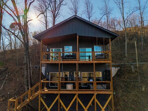Une cabane en bois à plusieurs niveaux, dotée d’un balcon à l’étage supérieur et entourée d’arbres.