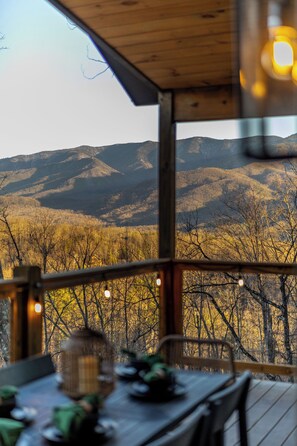 Une terrasse en bois avec une table dressée pour le repas, offrant une vue sur un paysage montagneux.