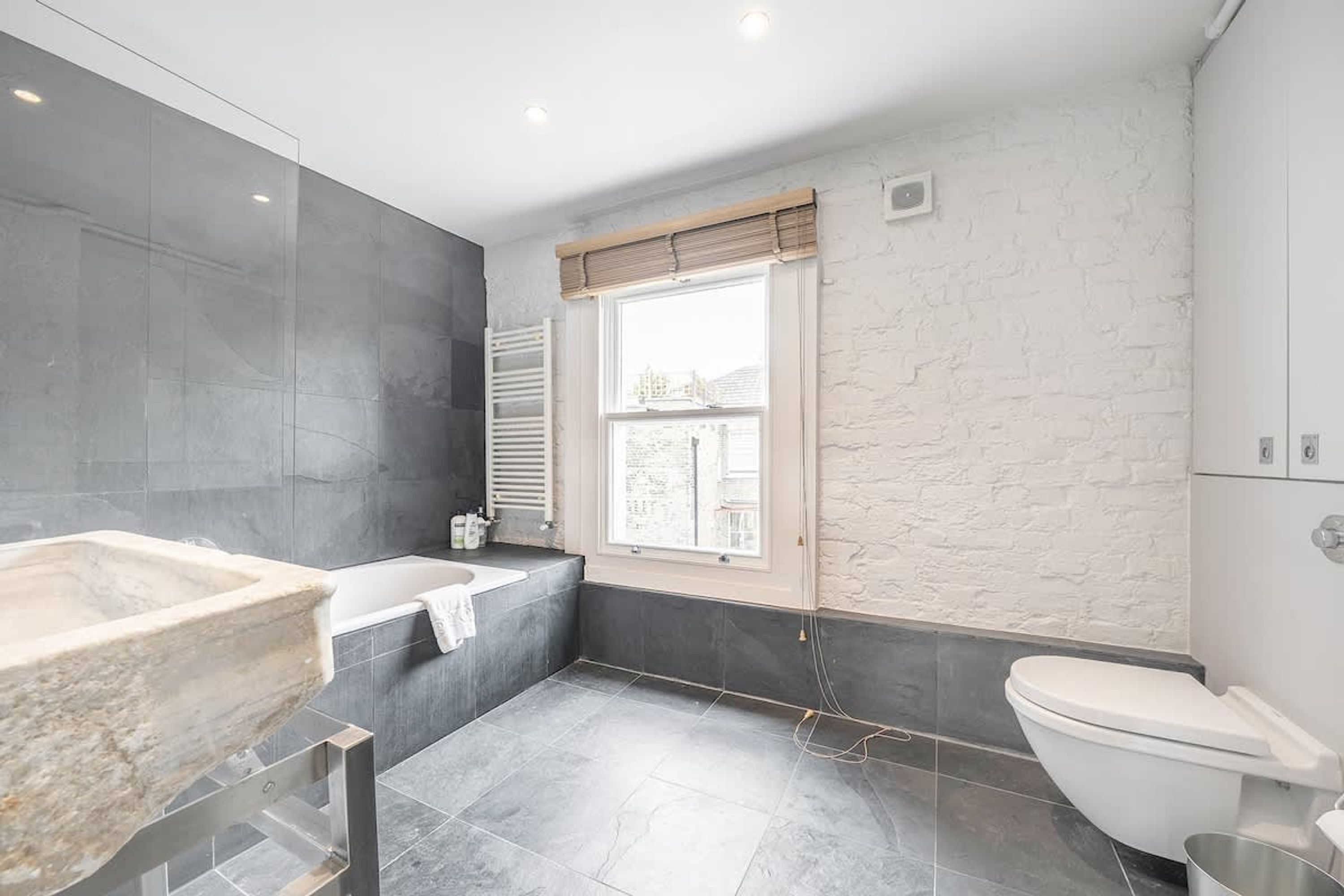 A modern bathroom with a stone sink, a bathtub, and a toilet.