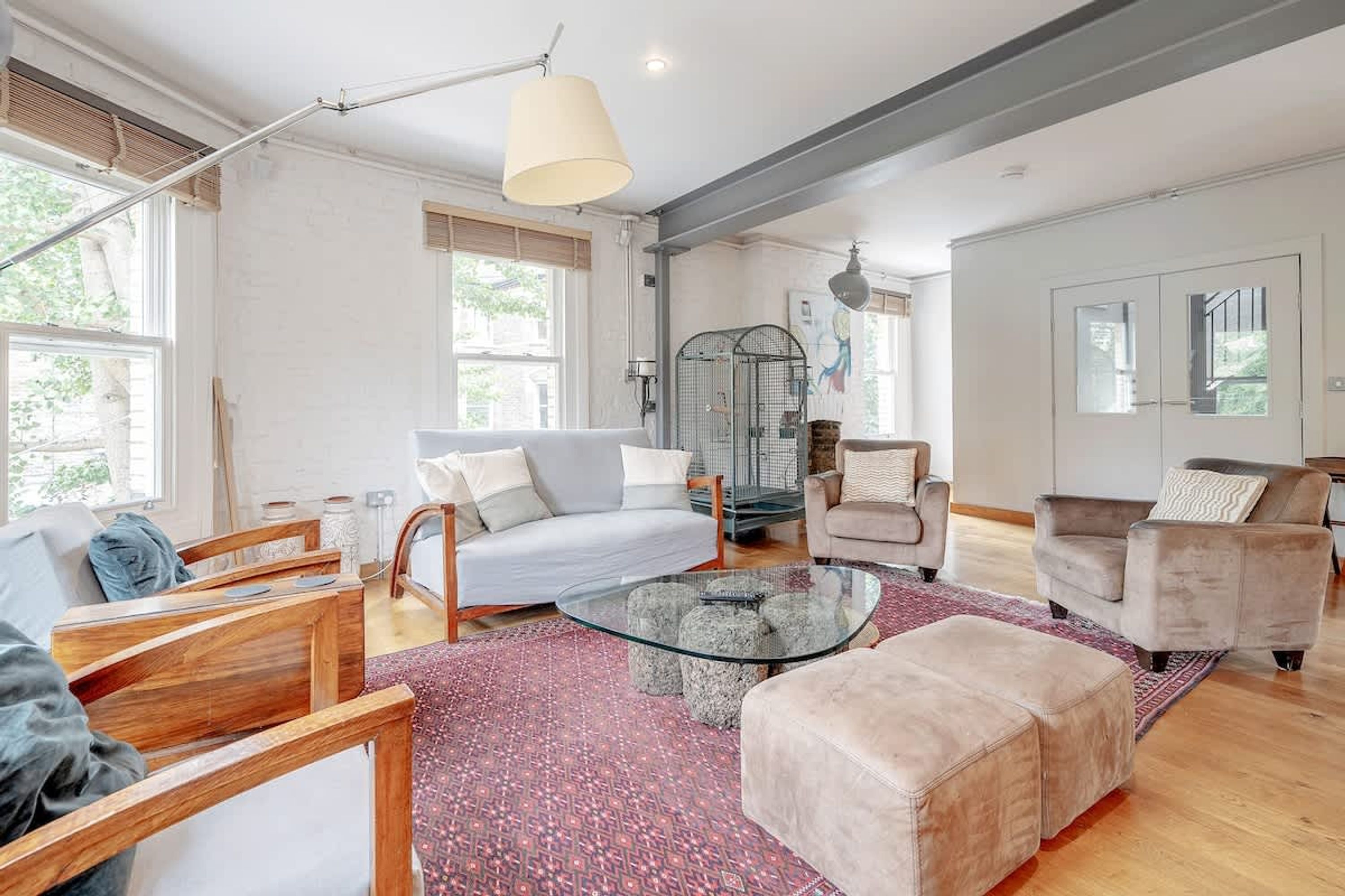 A spacious living room with a large window, a glass coffee table, a sofa, and a chair.