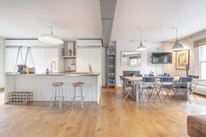A modern kitchen with a central island, bar stools, and a dining area with foldable chairs. - Experience London in amazing reconverted Gin house (London)