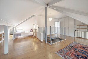 A spacious attic bedroom with a large bed, a wooden floor, a white railing, and a colorful rug. - Experience London in amazing reconverted Gin house (London)