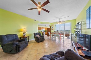 A spacious living room with a large sofa, a smaller armchair, and a dining area with a table and chairs. There is a ceiling fan, a TV, and a window with a view. - ⚓Water Views + Fishing Dock | Walk to the Beach |  Navy Cove Harbor 1209⚓ (Fort Morgan)