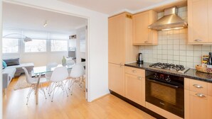 Eine moderne Küche mit Holzausstattung, einem Gasherd und einem Backofen. Ein Essbereich mit einem Glastisch und weißen Stühlen ist ebenfalls vorhanden.