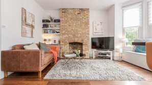 A living room with a brick fireplace, a sofa, a coffee table, and a television. - Modern   Scandi-style 2bed facing Vauxhall Park (Greater London)