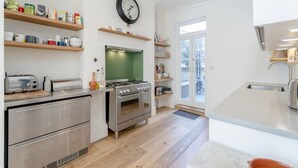 A modern kitchen with stainless steel appliances, wooden shelves, and a green backsplash. - 3bed House for an Authentic stay near river metro (Greater London)