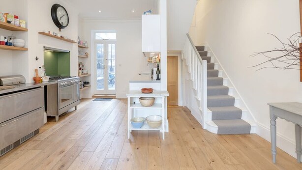 A spacious kitchen with modern appliances, a central island, and a staircase leading to a loft bedroom. - 3bed House for an Authentic stay near river metro (Greater London)