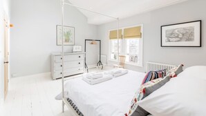 A bright bedroom with a bed, a dresser, a chair, and a window with a view. - 3bed House for an Authentic stay near river metro (Greater London)