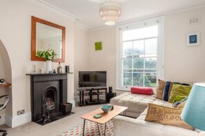 Una sala de estar con chimenea, televisor, sofá y un ventanal grande.