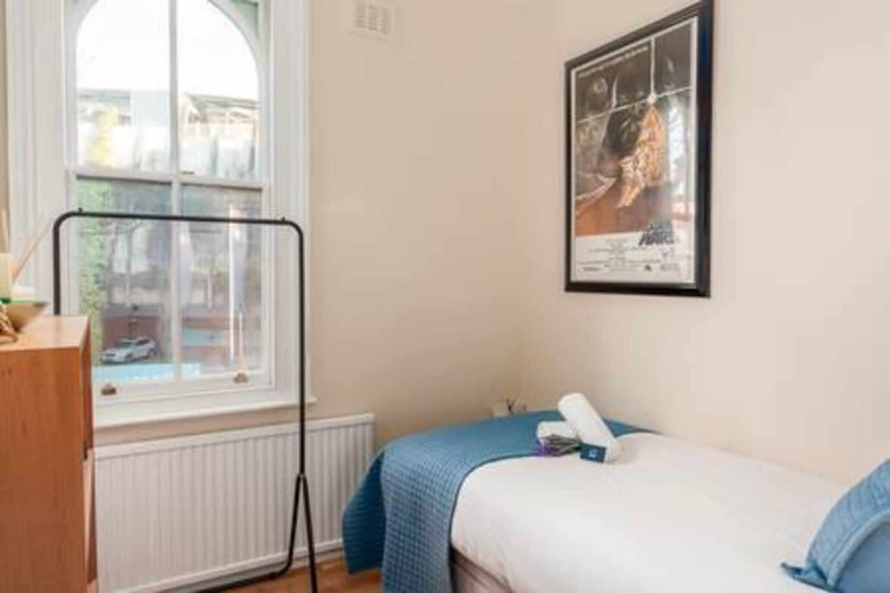 Une chambre à coucher avec un lit, une fenêtre, un radiateur et un tableau encadré au mur.