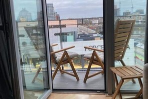 A balcony with two wooden chairs and a small table, overlooking a cityscape with buildings and a bridge. - Feel at home in a modern   spacious 1bed by river (Greater London)
