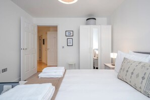 A hotel room with a bed, a wardrobe, a desk with a lamp, and a door leading to another room. - Feel at home in a modern   spacious 1bed by river (Greater London)