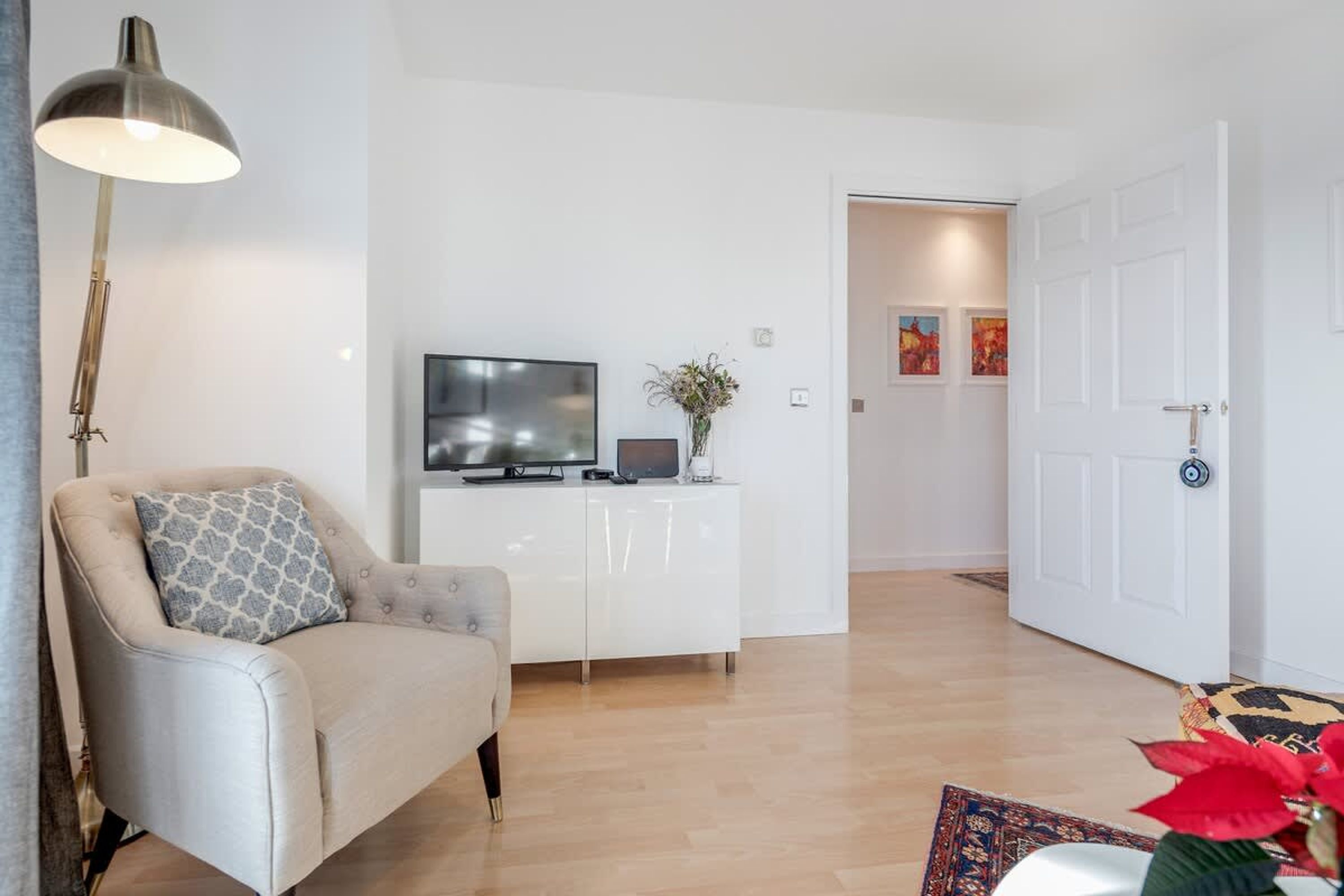 Un salon moderne avec un canapé, un téléviseur, un meuble blanc et une porte donnant sur une autre pièce.