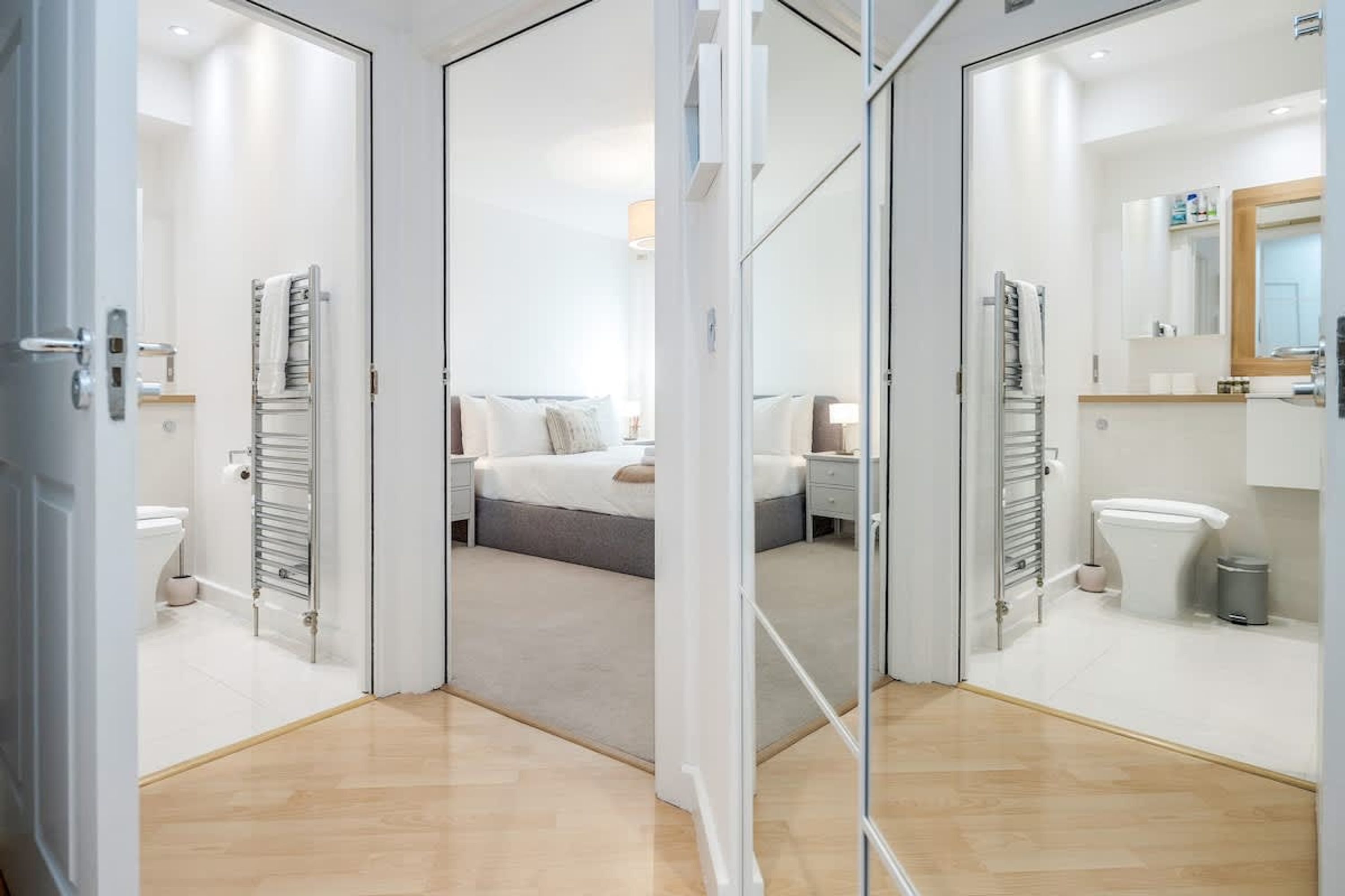 Una camera d'albergo moderna con un divisorio in vetro, un letto con lenzuola bianche, un comodino, uno specchio e un bagno con il water e il lavandino.