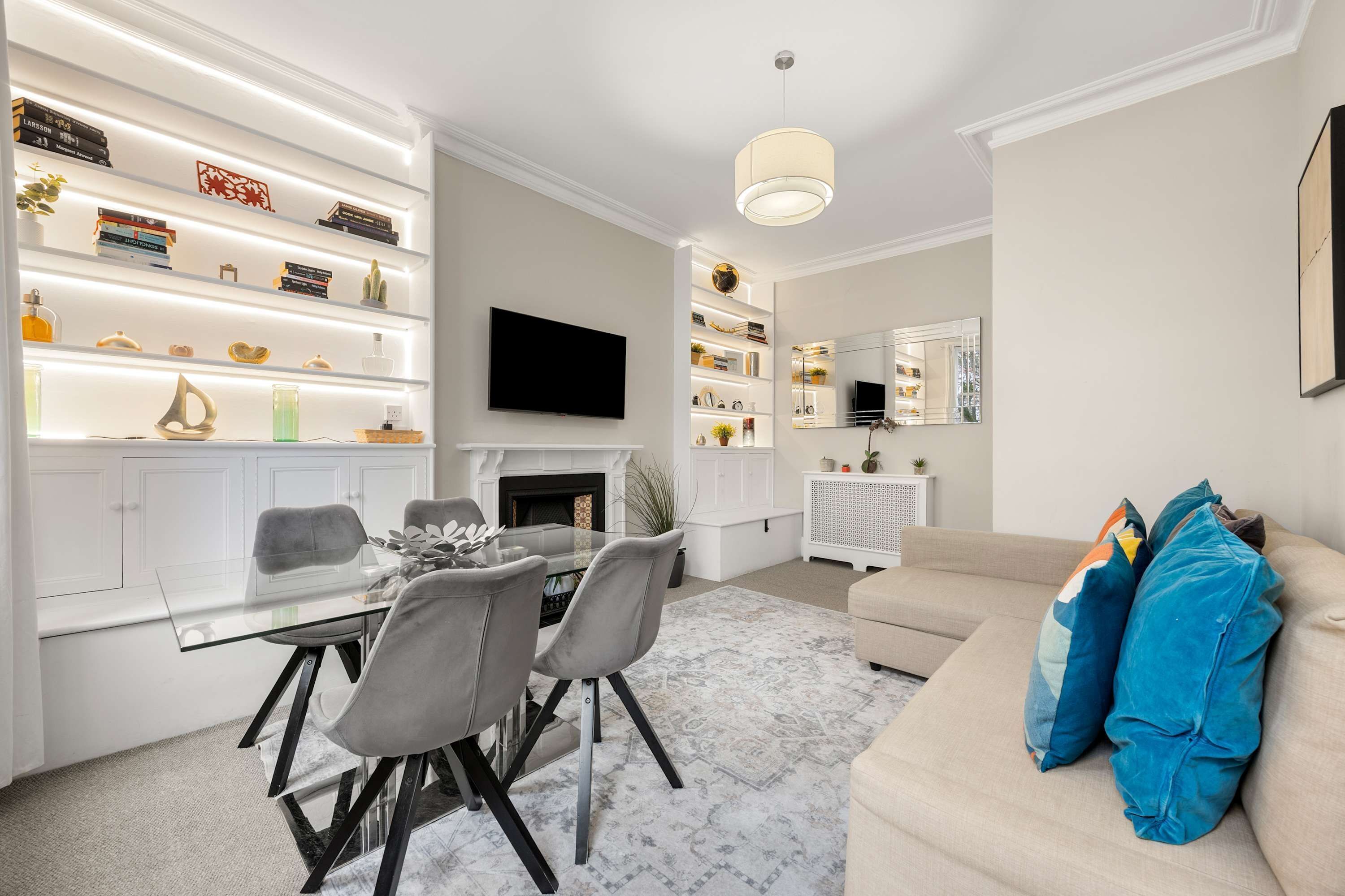 Una sala de estar moderna con una mesa de comedor de vidrio, sillas grises, un sofá beige y una chimenea.