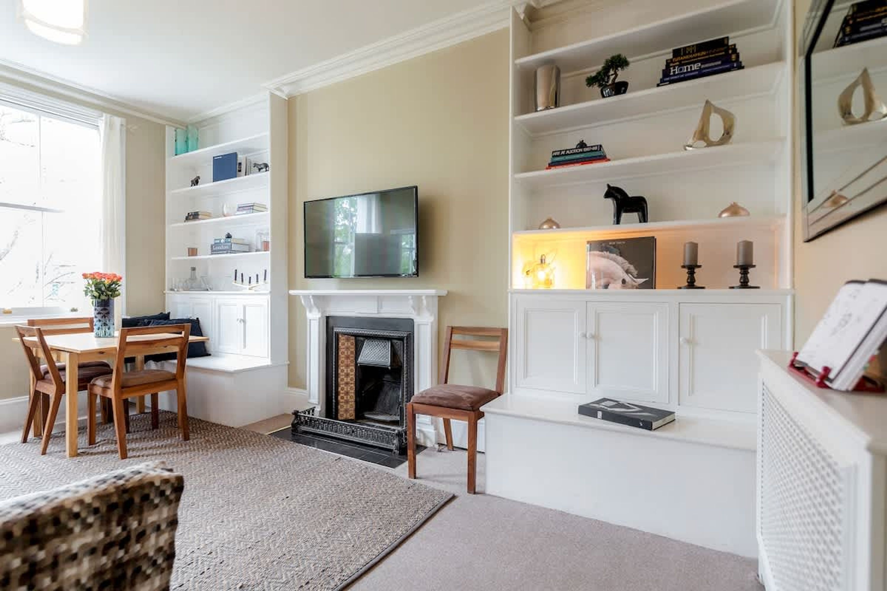 A living room with a fireplace, a television, a bookshelf, and a dining area with chairs and a table.