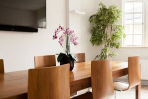 A dining area with a wooden table and chairs, a potted orchid, and a large green plant. - Modern   Stylish 2bed 2bath close to Kings Road (London)