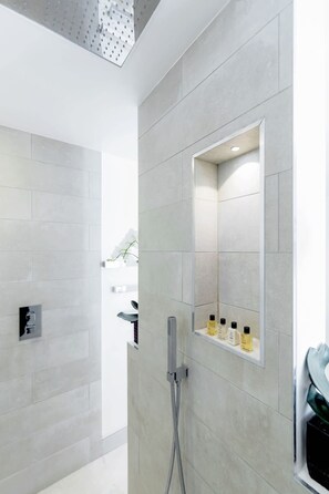 A modern bathroom with a shower, a mirror, and a shelf with toiletries. - Modern   Stylish 2bed 2bath close to Kings Road (London)
