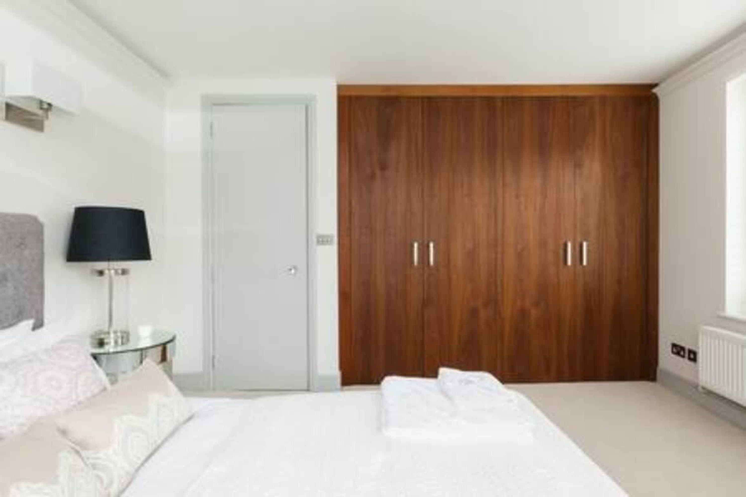 A bedroom with a bed, a nightstand, a lamp, a wardrobe, and a radiator.