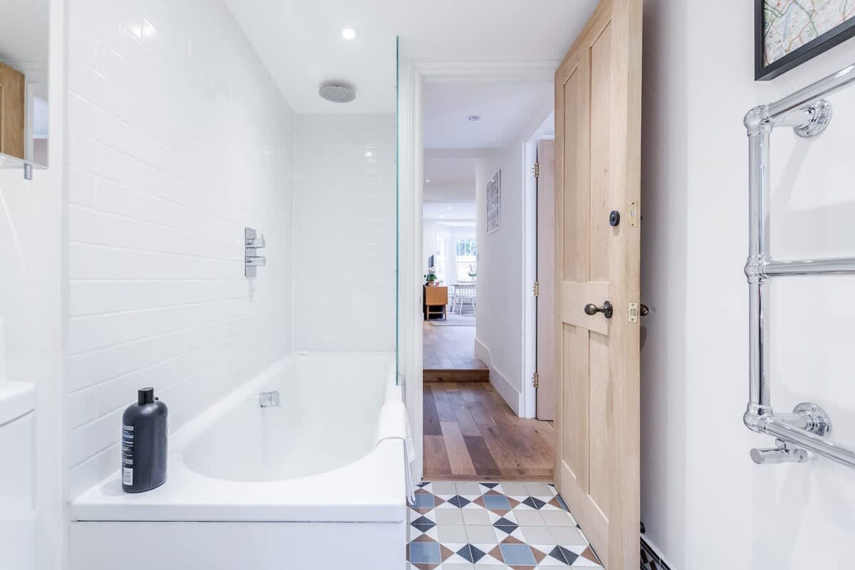A modern bathroom with a white bathtub, a glass shower enclosure, and a wooden door.