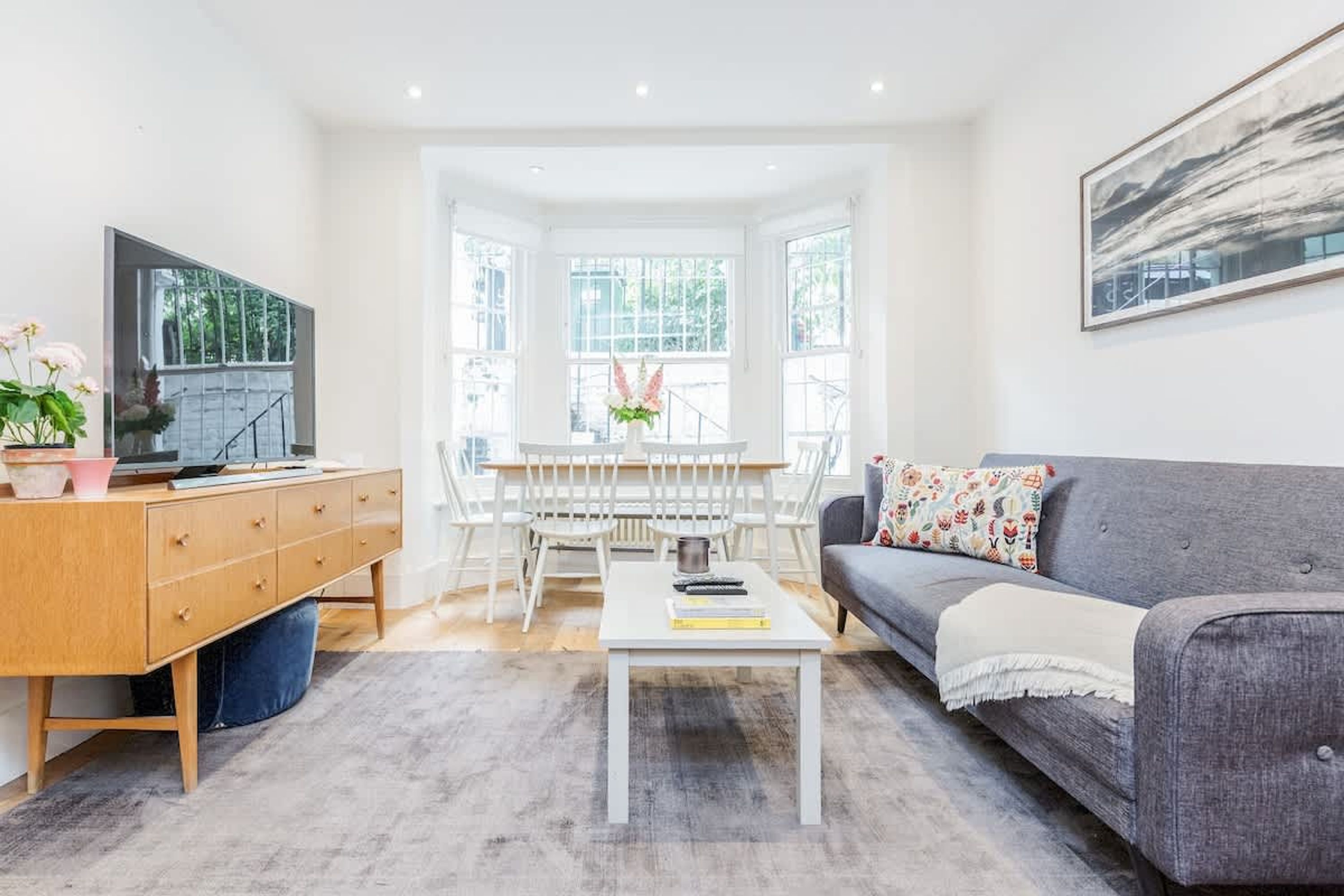 Un salon moderne avec un canapé gris, une table basse blanche, un meuble en bois et un coin repas comprenant des chaises et une table blanches.