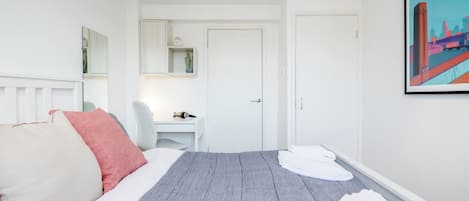 A hotel room with a bed, a desk, and a chair. There is a door and a painting on the wall.