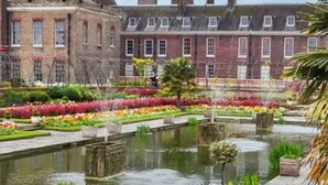 Un bâtiment historique à la façade symétrique, doté d’une cour centrale avec une fontaine et d’un jardin bien entretenu agrémenté de parterres de fleurs aux couleurs vives.