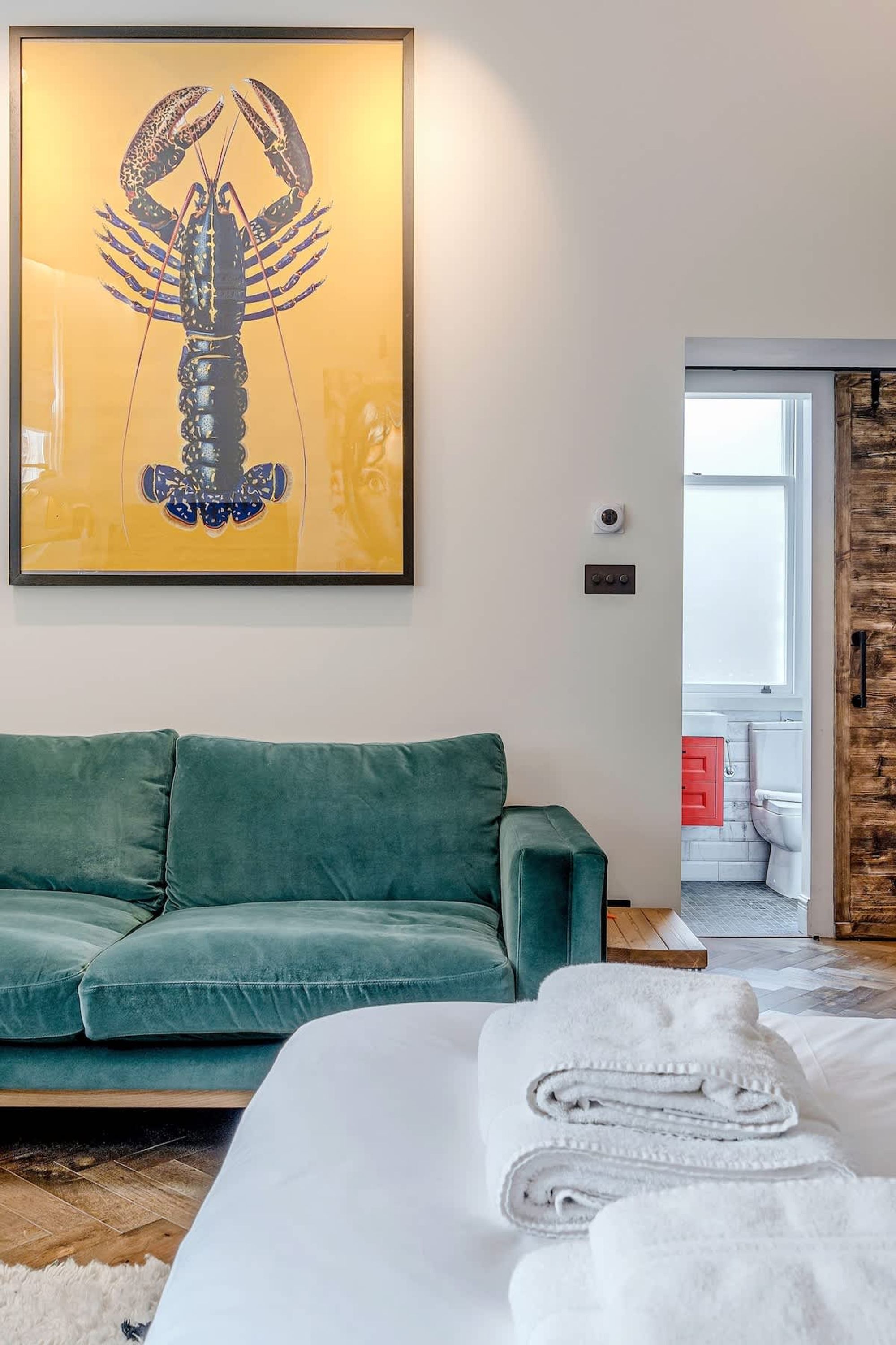 A room with a green sofa, a bed with white linens, and a lobster-themed artwork on the wall.