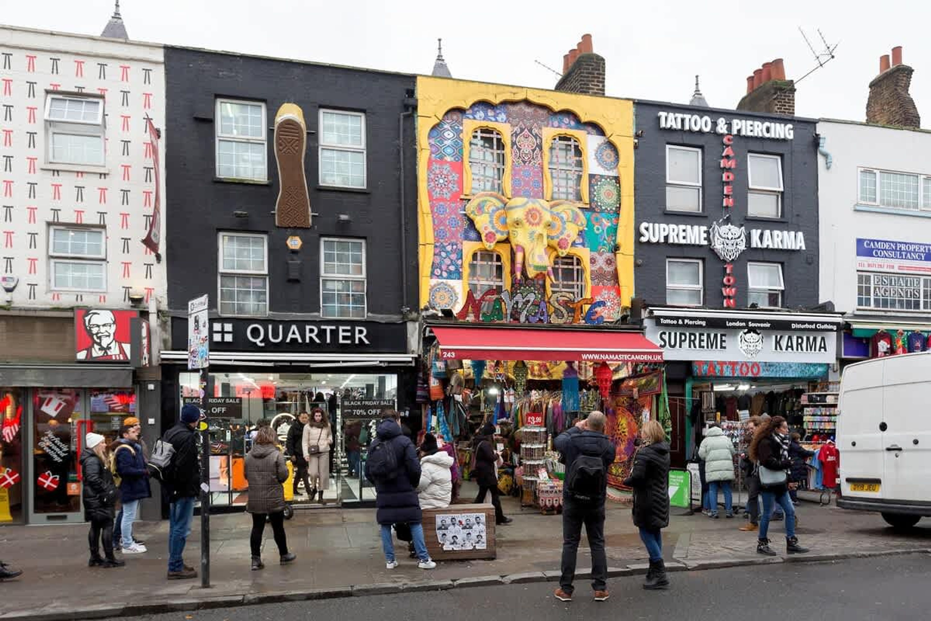 A street with various shops including a tattoo and piercing shop, a KFC, and a Quarter store.