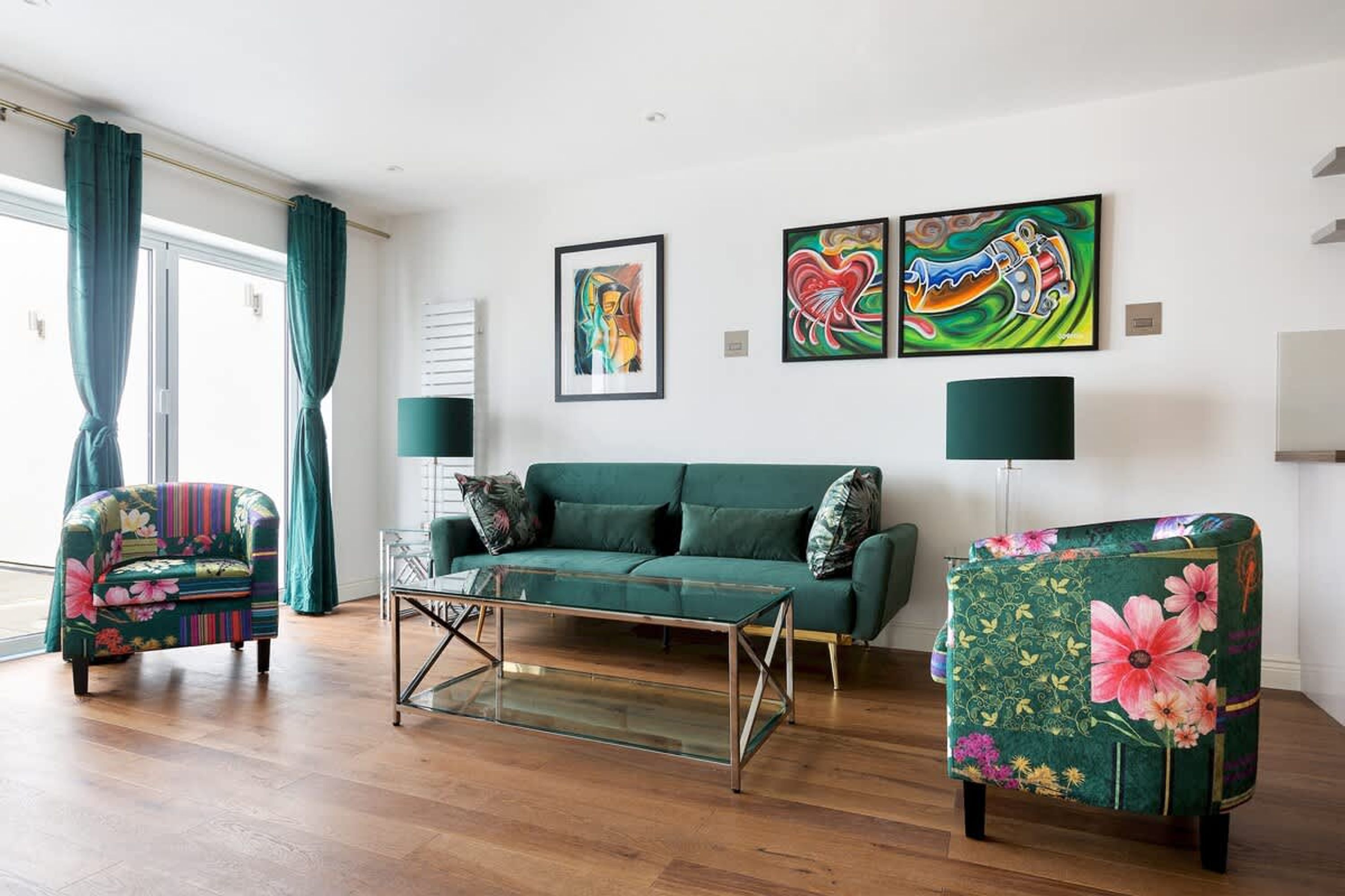 Ein Wohnzimmer mit einem grünen Sofa, zwei Sesseln, einem Glastisch und zwei Bildern an der Wand.