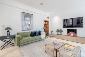 A modern living room with a green sofa, a coffee table with suitcases, a bookshelf, and a TV on the wall. - Spacious   modern 2bed 2 5bath in Pimlico-Victoria (Greater London)