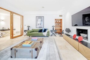 A modern living room with a green sofa, a coffee table with suitcases, a fireplace, and a television on the wall. - Spacious   modern 2bed 2 5bath in Pimlico-Victoria (Greater London)